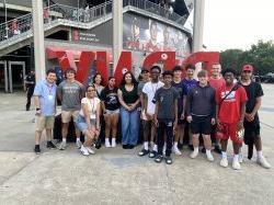 Students standing and smiling in two rows outside of a soccer stadium.